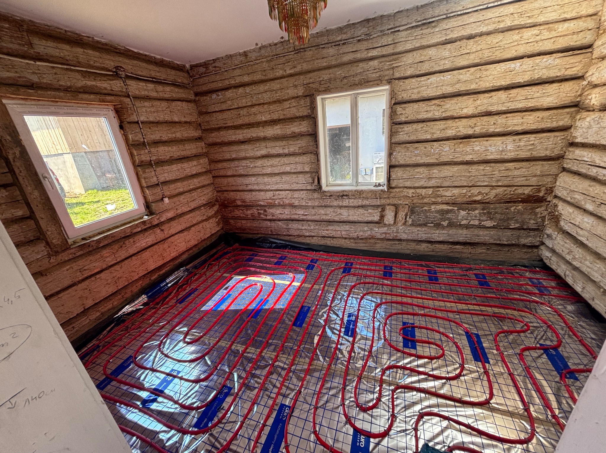 Czerwone rury ogrzewania podłogowego ułożone na folii refleksyjnej w drewnianym domu, widok z góry, etap instalacji przed wylewką.
