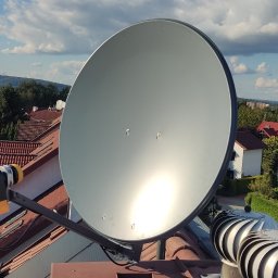 HORYZONT Montaż Serwis Anten TV Kraków - Antena satelitarna zamontowana na dachu domu z widokiem na okoliczną zabudowę i błękitne niebo z chmurami.