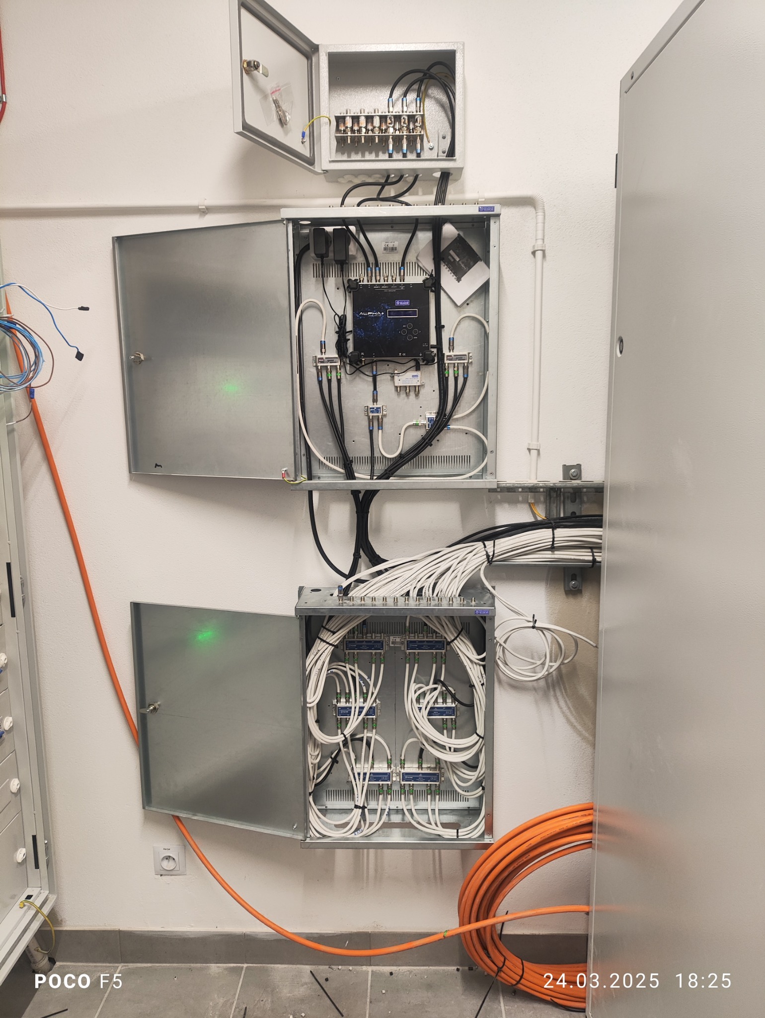 Rozdzielnice antenowe i okablowanie wewnątrz szaf metalowych na ścianie, widoczne złącza, kable koncentryczne i przewody światłowodowe.