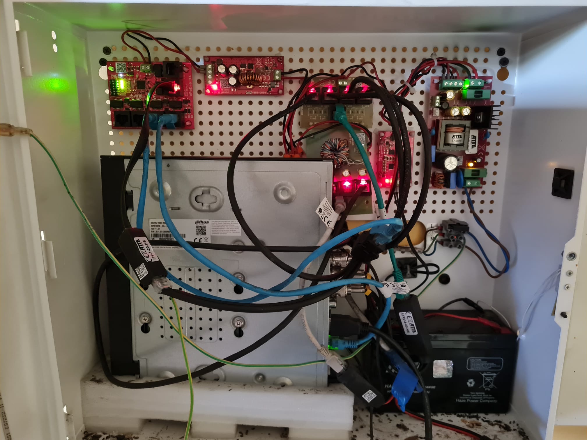 Wnętrze szafki z zamontowanym rejestratorem cyfrowym Dahua, zasilaczami, modułami PoE i akumulatorem, połączonymi kablami Ethernet i zasilającymi. Widoczne diody LED sygnalizujące pracę urządzeń.