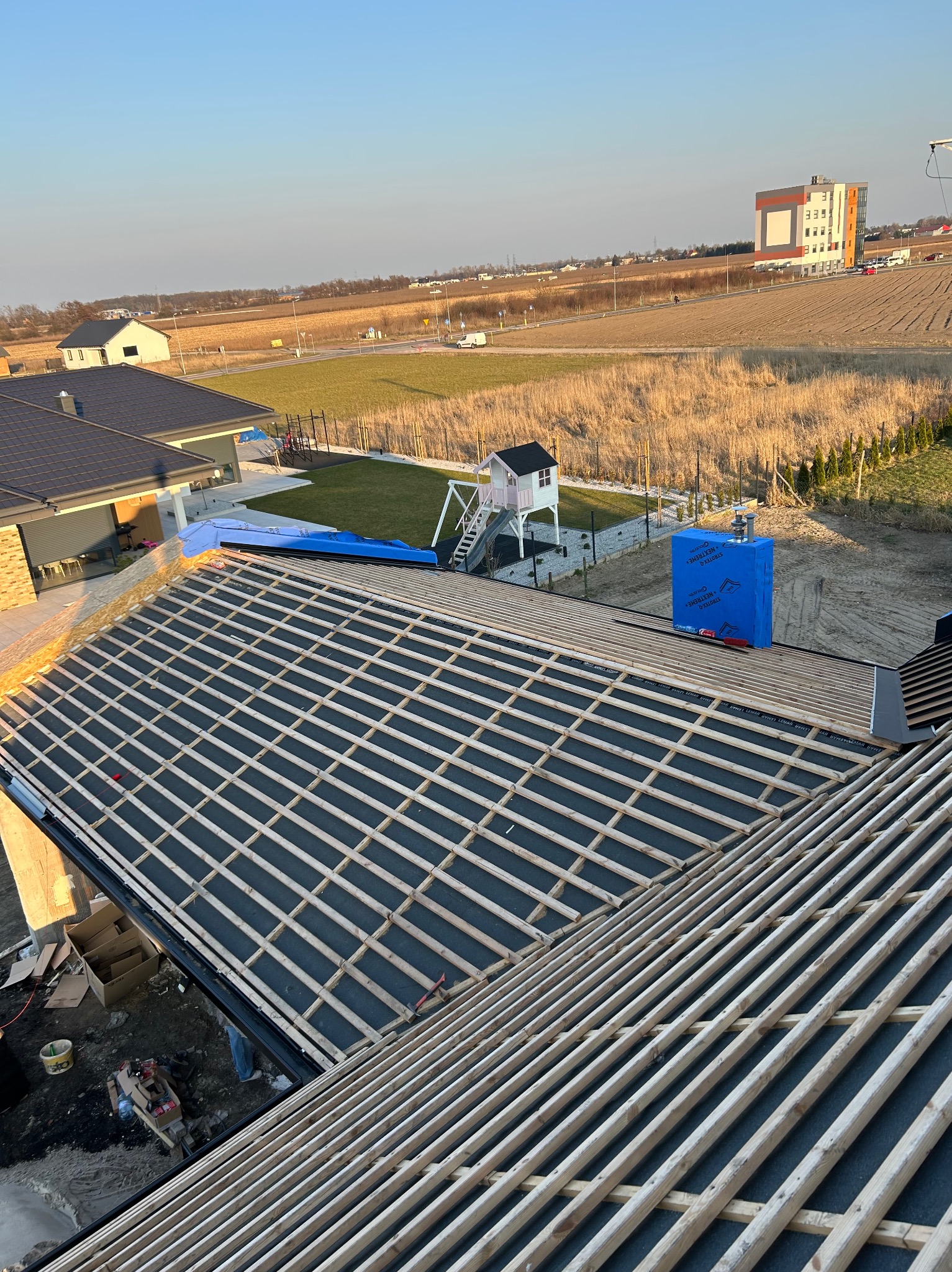Konstrukcja dachu z łatami i membraną w Gnieźnie, widok z góry na budowę domu jednorodzinnego z elementami placu zabaw w tle.