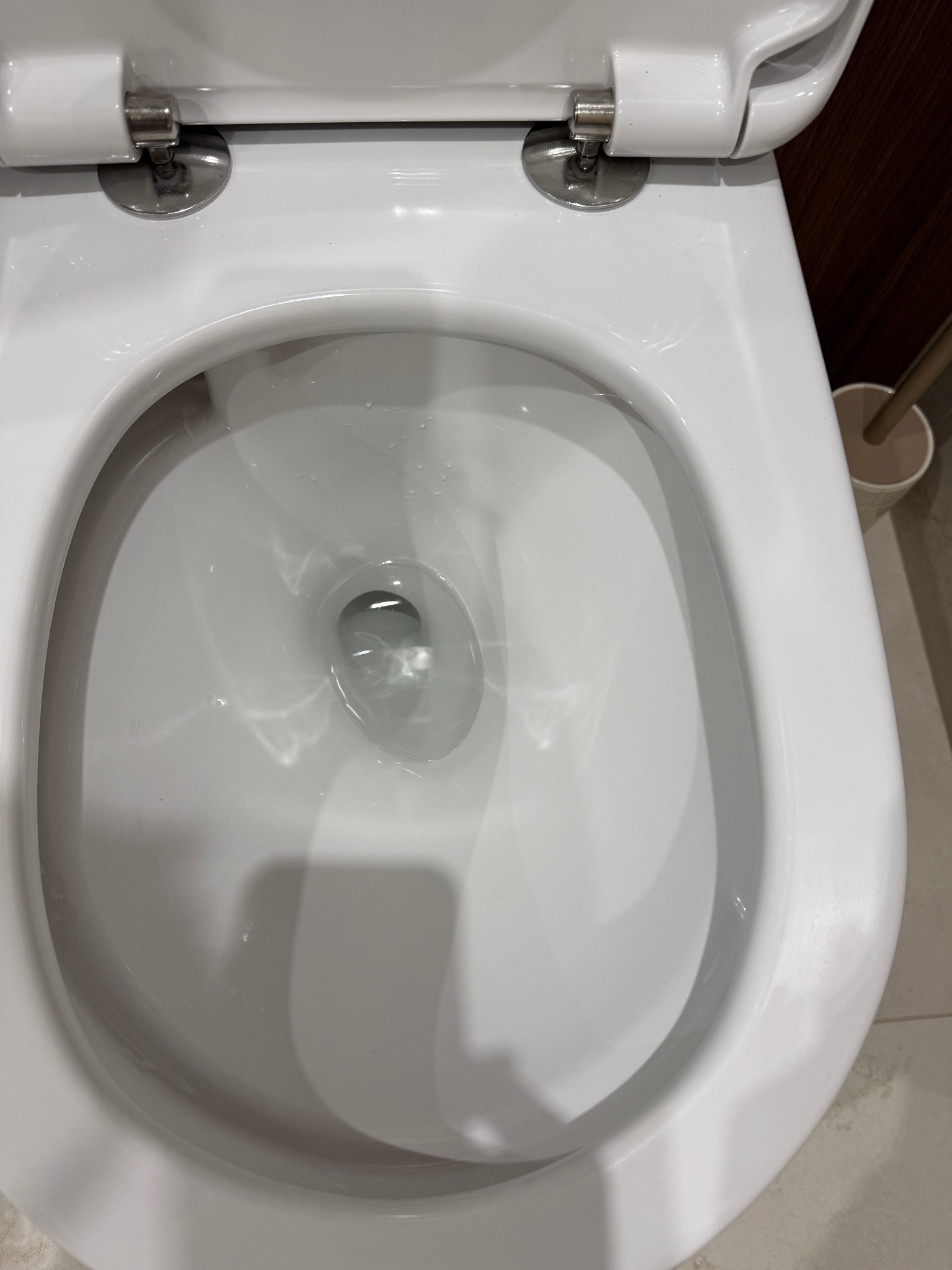 Biała, ceramiczna muszla klozetowa z otwartą klapą, wypełniona czystą wodą. Widoczny fragment szczotki do WC. Higieniczna czystość w łazience.