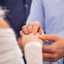 Zatrzymane w Czasie - Moment zakładania obrączki podczas ceremonii ślubnej, widoczna dłoń panny młodej i pana młodego, zegarek na ręce pana młodego.