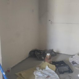 ŁUKASZ PIERSZCHAŁA GUM-BUD - Pokój w trakcie przygotowań do malowania: zabezpieczona podłoga folią, drabina i narzędzia malarskie widoczne, ściany zagruntowane, gotowe do nałożenia farby.