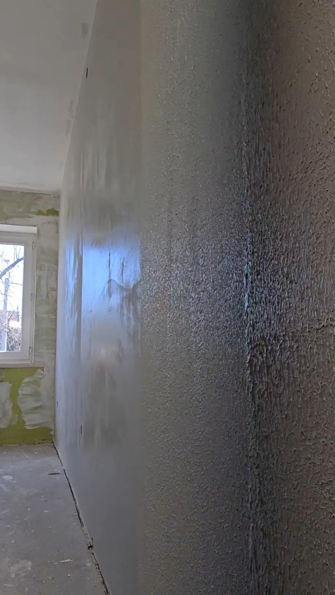 Ściana po nałożeniu dekoracyjnej struktury w Rawiczu. Widoczny fragment okna i surowego stanu pomieszczenia przed wykończeniem. Teksturowana powierzchnia odbija światło.