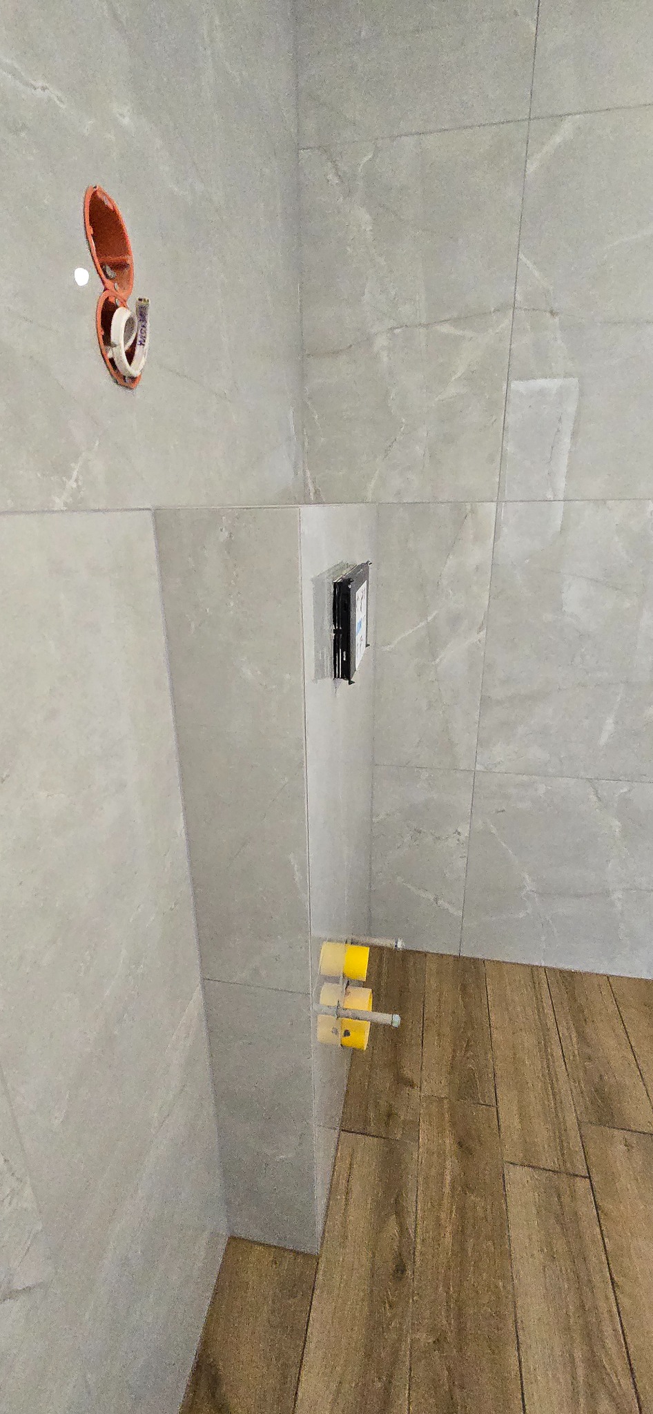 Wykończona ściana i podłoga w łazience w Rawiczu, z widocznymi instalacjami hydraulicznymi i elektrycznymi przed montażem armatury. Jasne płytki imitujące marmur.