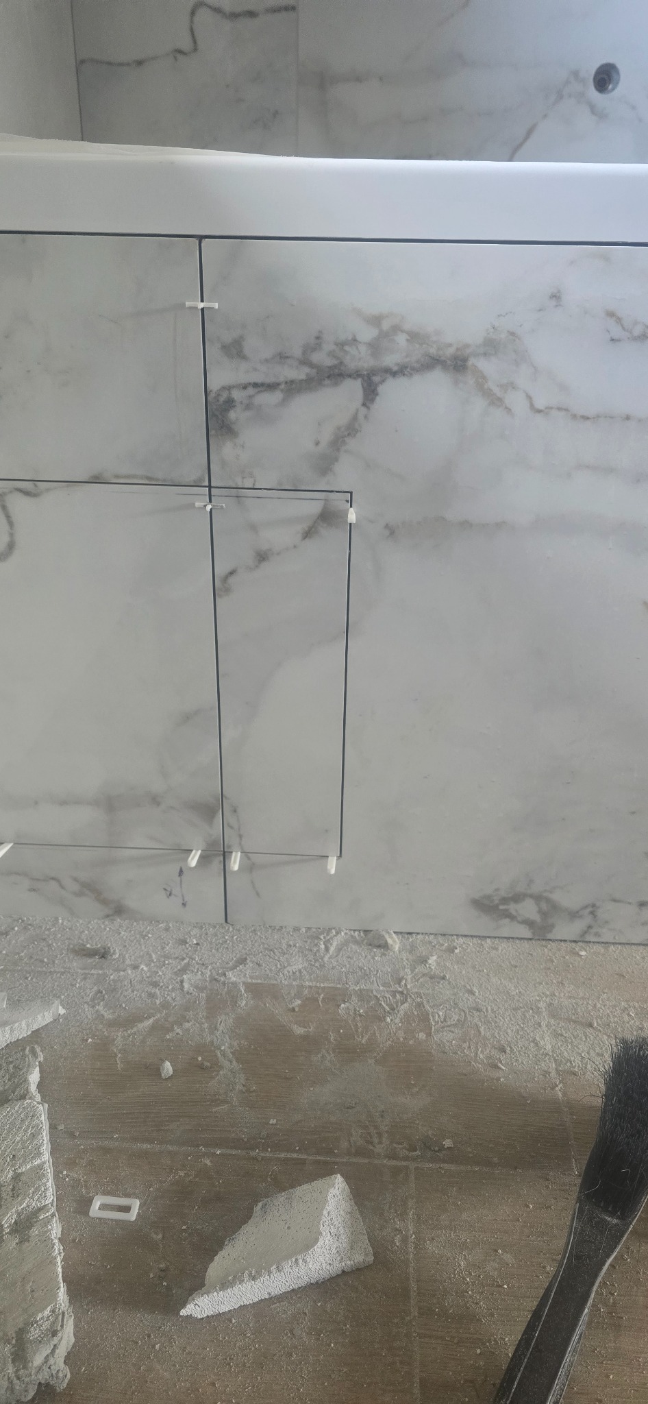 Układanie płytek marmuropodobnych na ścianie, z użyciem krzyżyków dystansowych. Fragment posadzki z resztkami zaprawy i narzędziem. Detal z remontu.