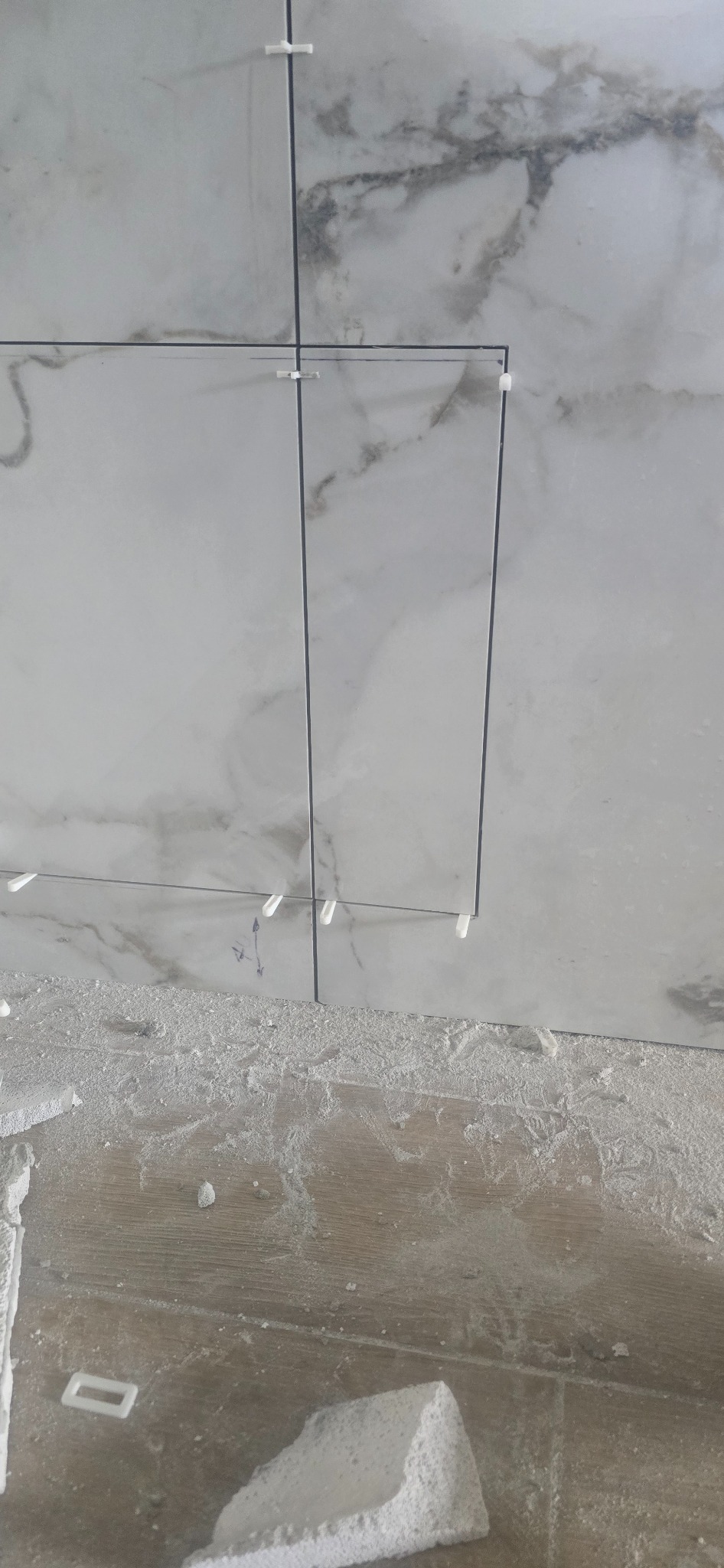 Układanie płytek marmuropodobnych z użyciem krzyżyków dystansowych. Widoczny fragment podłogi z resztkami zaprawy.