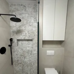 Nowoczesna łazienka z kabiną prysznicową typu walk-in, czarną armaturą i szafką wiszącą nad toaletą. Płytki z wzorem.