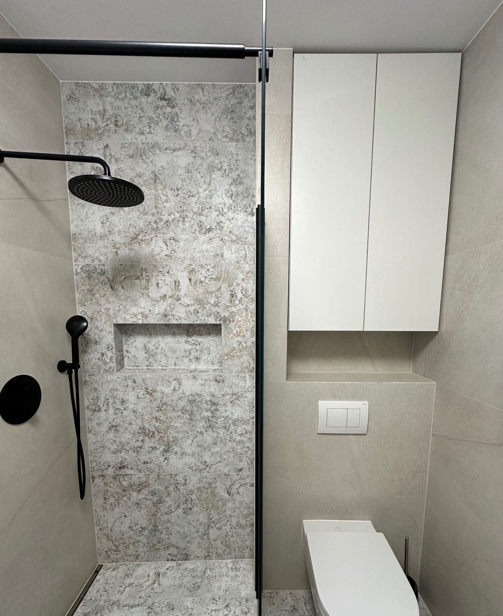 Nowoczesna łazienka z kabiną prysznicową typu walk-in, czarną armaturą i szafką wiszącą nad toaletą. Płytki z wzorem.