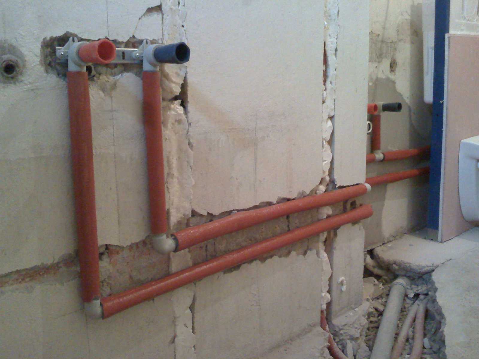 Instalacja wodna z rur w kolorze ceglastym, częściowo zamontowana w surowej ścianie podczas remontu łazienki, widoczne otwory na baterie i przyłącza.