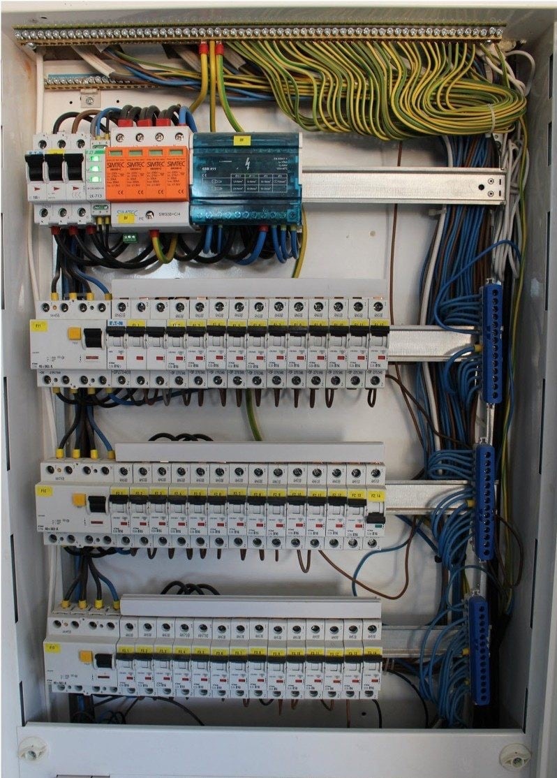 Rozdzielnia elektryczna z zainstalowanymi bezpiecznikami, ogranicznikami przepięć i uporządkowanymi przewodami wewnątrz białej obudowy.