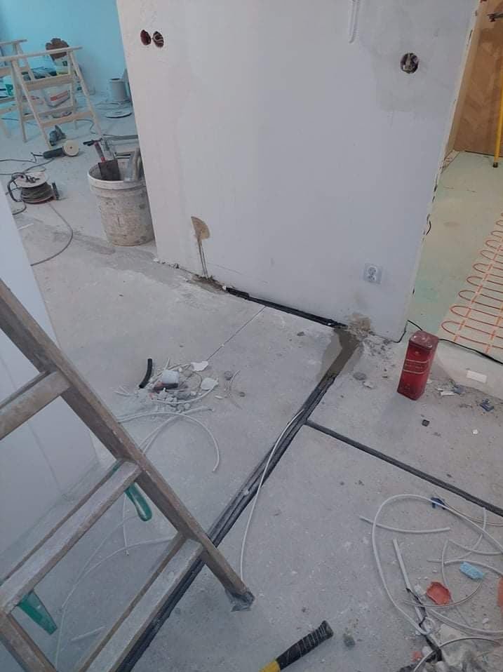 Wnętrze w trakcie prac elektrycznych: kable w podłodze, puszki w ścianie, drabina, narzędzia. Widoczne elementy instalacji ogrzewania podłogowego.