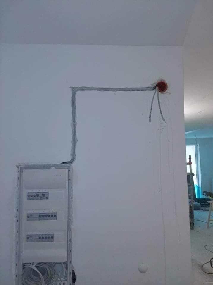 Wnęka pod rozdzielnicę i bruzdy pod kable elektryczne w ścianie, przygotowane do dalszych prac instalacyjnych. Widoczne przewody wychodzące z puszki.