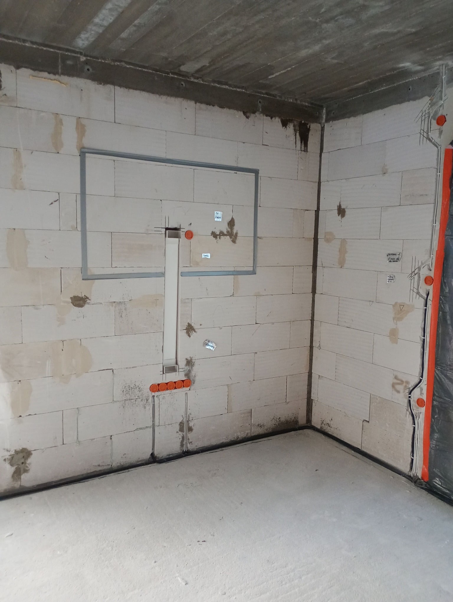 Wewnętrzna instalacja elektryczna w surowym pomieszczeniu. Widoczne kable w peszlach, puszki instalacyjne i ramy podtynkowego montażu. Ściany z betonu komórkowego.