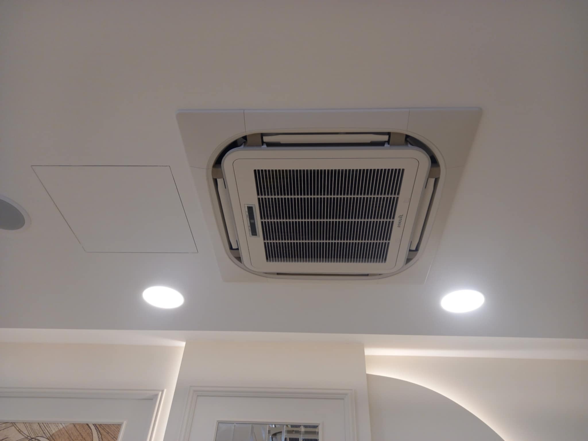 Kasetonowa klimatyzacja sufitowa wkomponowana w eleganckie wnętrze, widok z dołu, z dwoma punktowymi lampami LED w pobliżu.