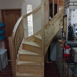 Usługi stolarskie Andrzej Halupczok - Jasne, drewniane schody kręte z balustradą wewnątrz domu, widoczne na tle ściany z luksferami i drewnianych drzwi. Elementy wykończeniowe w surowym drewnie.