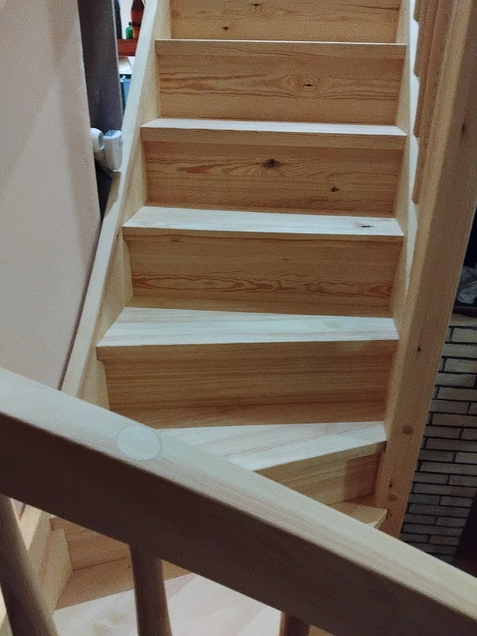 Jasne, drewniane schody z widocznym rysunkiem słojów, prowadzące w górę. Widoczne fragmenty ściany i ceglanej obudowy. Ujęcie z dołu, podkreślające stopnie.
