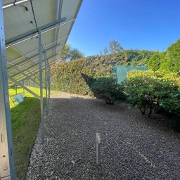 KONSTANTYN PYSHNIAK - Widok na ogród z panelami słonecznymi, gdzie ścieżka wysypana jest drobnymi kamieniami, a w tle widać zielony żywopłot i błękitne niebo.