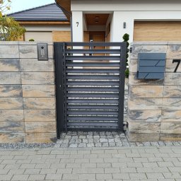 MUROWANE KARILO - Nowoczesna brama z poziomych profili, osadzona między słupkami z bloczków w odcieniach beżu i szarości. Widoczny dom z numerem 7, skrzynka na listy i domofon.