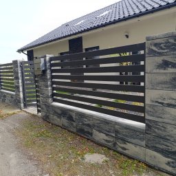 MUROWANE KARILO - Nowoczesne ogrodzenie z betonowych bloczków o marmurkowym wzorze i poziomych, czarnych przęseł. Widoczna furtka i skrzynka pocztowa, dom w tle.