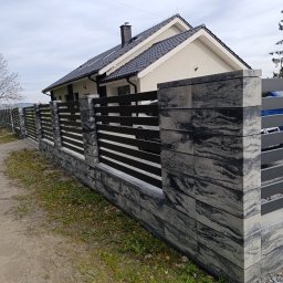 MUROWANE KARILO - Nowoczesne ogrodzenie z betonowych bloczków w odcieniach szarości i czarnych, poziomych przęseł, na tle domu z ciemną dachówką w pochmurny dzień.