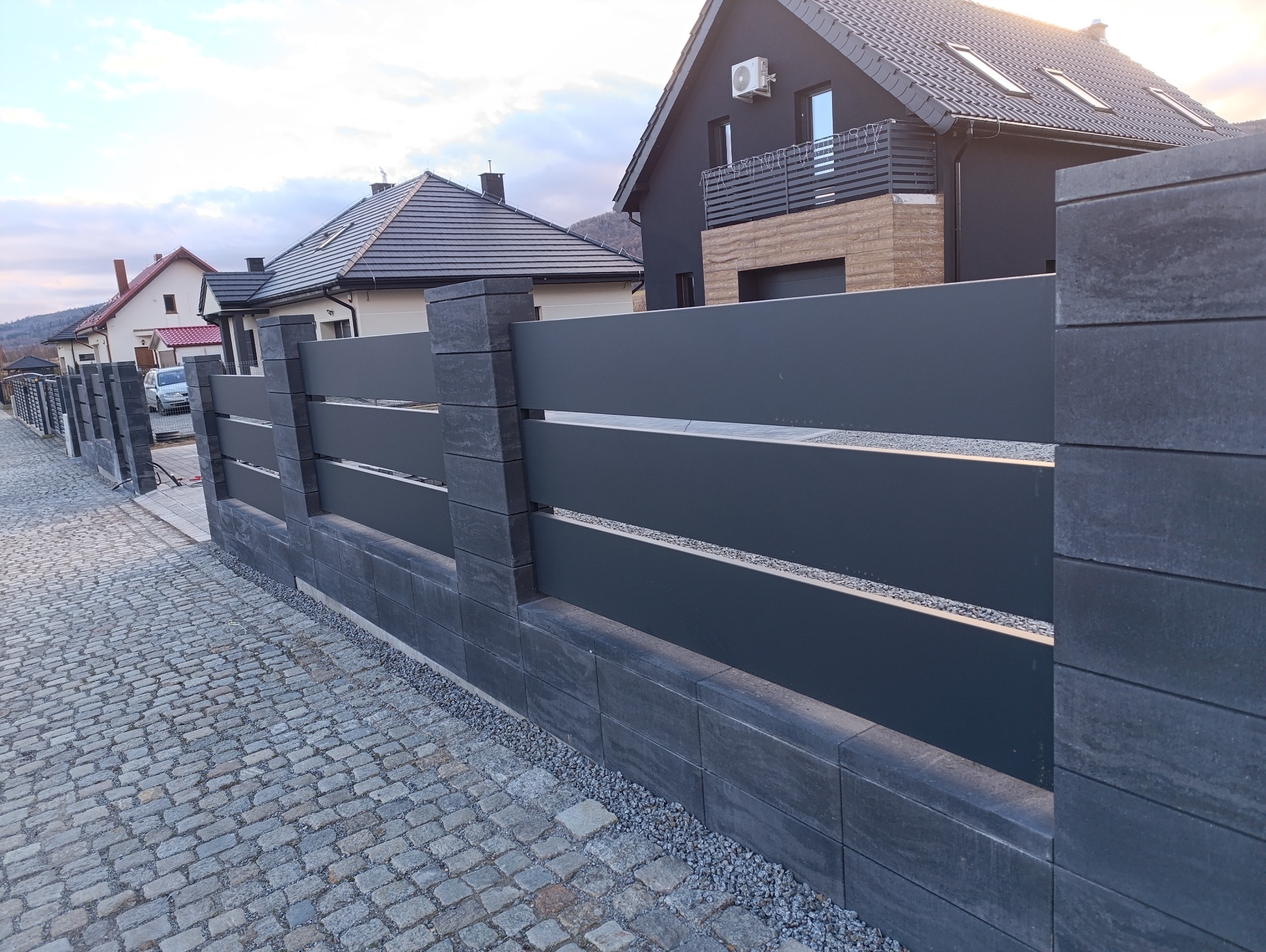 Nowoczesne ogrodzenie z szarego metalu i betonowych bloczków w Bielawie. Minimalistyczny design z poziomymi panelami i kamienną kostką brukową.