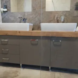 Szara szafka łazienkowa z drewnianym blatem i dwiema białymi umywalkami nablatowymi, chromowane nóżki i uchwyty. Minimalistyczny design, marmurowe płytki w tle.