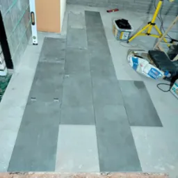 Układanie szarych płytek podłogowych z użyciem klipsów dystansowych w Płocku. Widoczny poziomica, lampa budowlana i zaprawa klejowa.