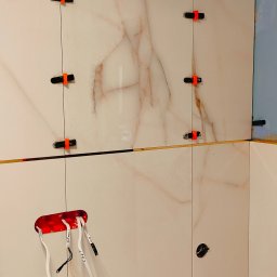 KONTUR ART SPÓŁKA Z OGRANICZONĄ ODPOWIEDZIALNOŚCIĄ - Montaż płytek imitujących marmur z użyciem klipsów poziomujących. Widoczne przewody elektryczne w puszce. Detal wykończenia łazienki w trakcie prac.
