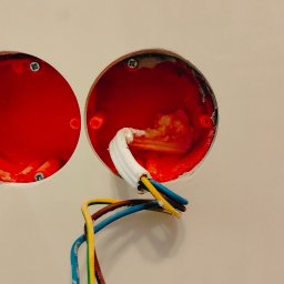 KONTUR ART SPÓŁKA Z OGRANICZONĄ ODPOWIEDZIALNOŚCIĄ - Dwa czerwone, okrągłe otwory w ścianie z wystającymi przewodami elektrycznymi. Widoczne ślady po szpachlowaniu wokół otworów. Ujęcie z bliska, oświetlenie naturalne.