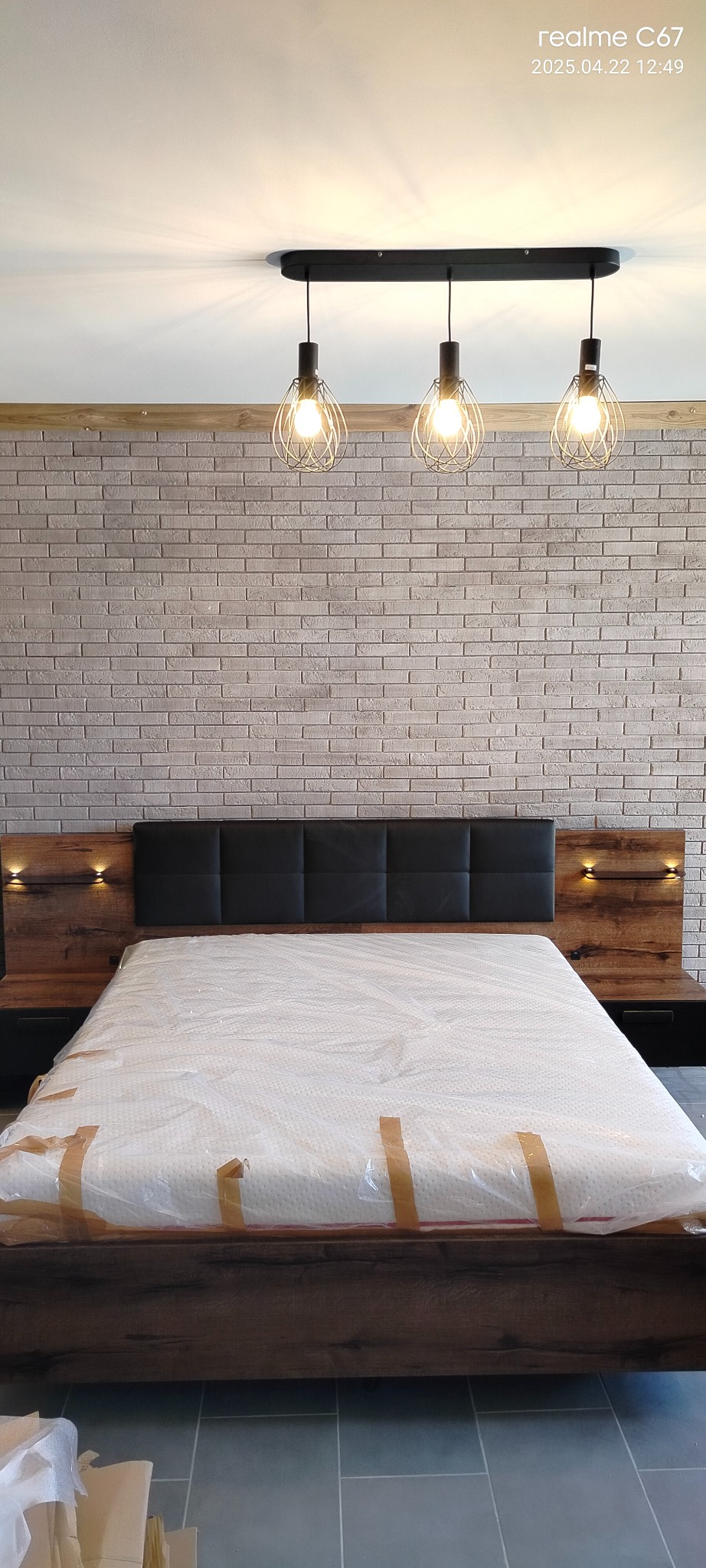 Nowoczesna sypialnia z łóżkiem w folii, ceglana ściana i lampy wiszące. Wykończenie wnętrza w stylu industrialnym, oświetlenie punktowe.