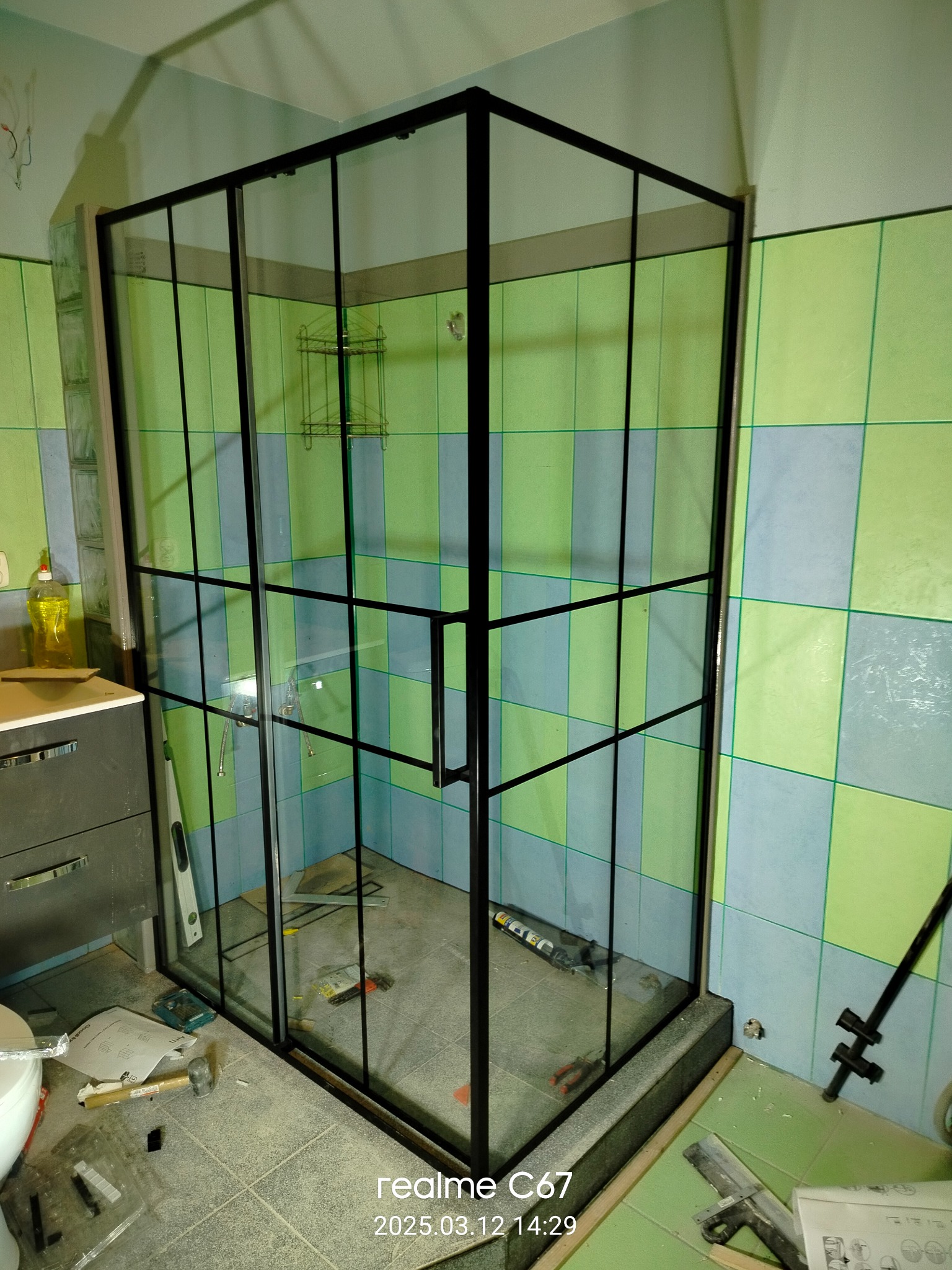 Montaż kabiny prysznicowej z czarnymi profilami w łazience z zielono-niebieskimi płytkami. Widoczne narzędzia i akcesoria montażowe. Ujęcie z bliska, prezentujące etap prac.