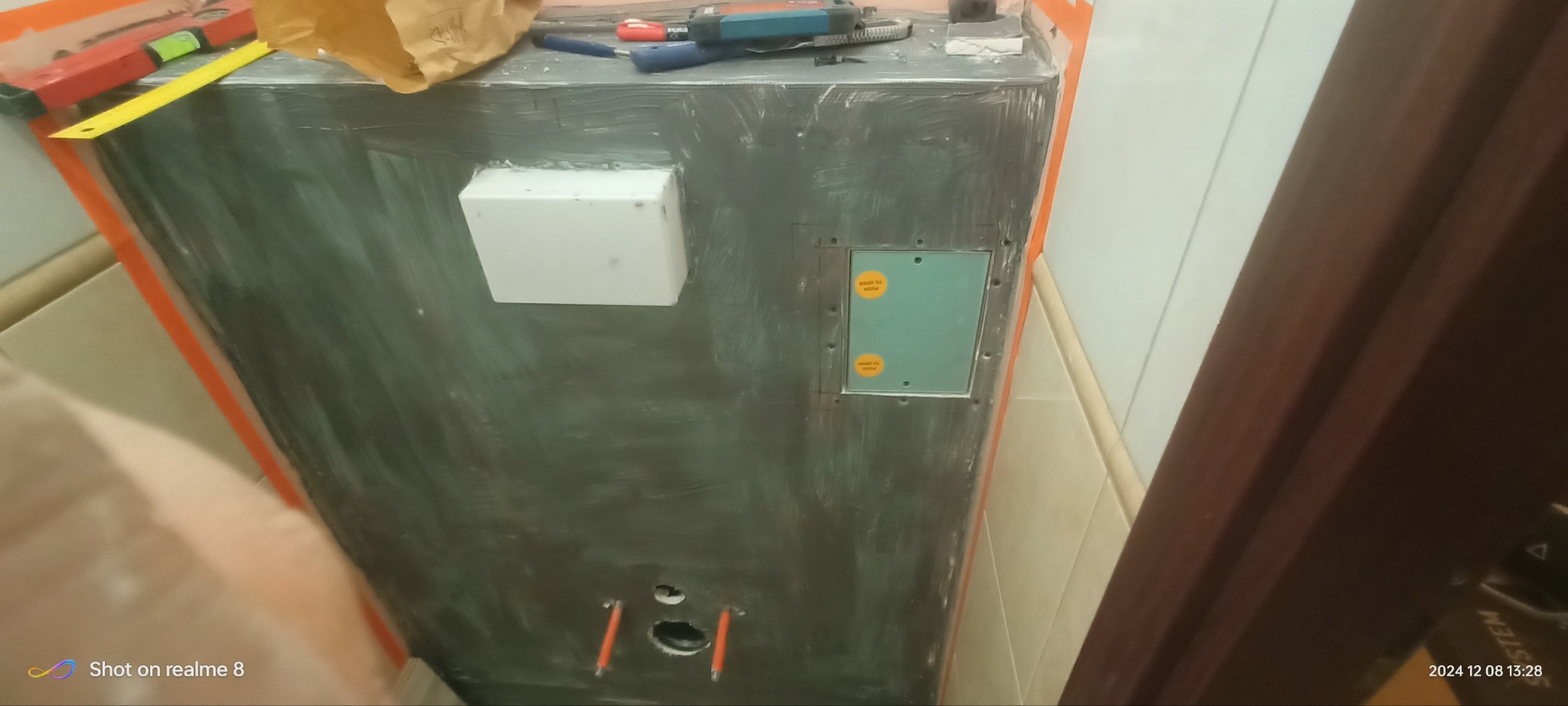 Obudowa stelaża WC w trakcie prac wykończeniowych: szpachlowanie, montaż rewizji. Widoczne narzędzia i poziomica. Detal z łazienki w trakcie remontu.