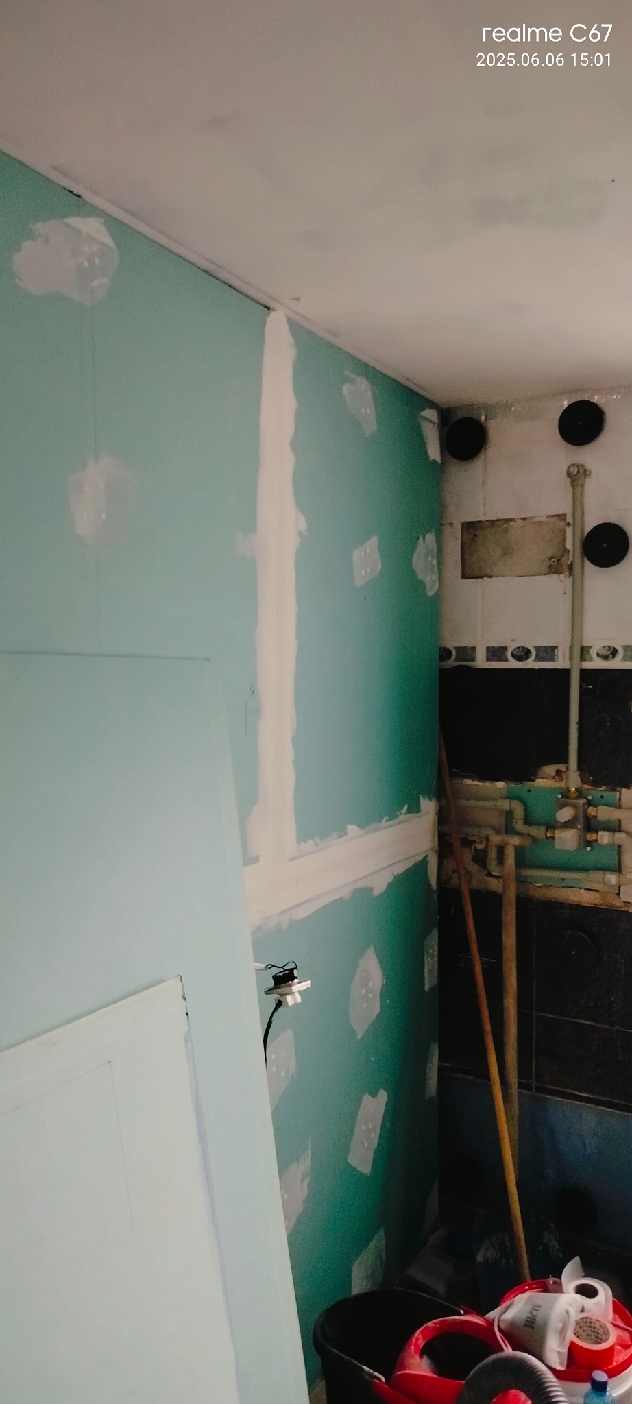 Narożnik remontowanej łazienki z płytami GK, częściowo wyszpachlowanymi ścianami i widoczną instalacją hydrauliczną. Ujęcie z dołu, widoczne narzędzia.