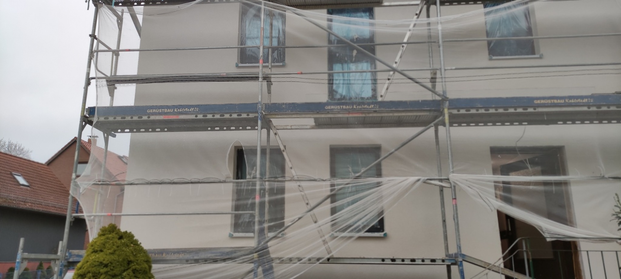 Elewacja domu w Northeim w trakcie malowania, zabezpieczona siatką ochronną i rusztowaniami.