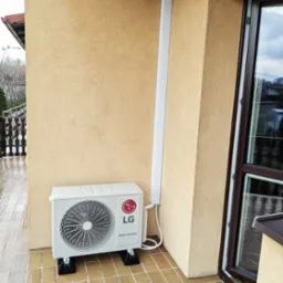 Zewnętrzna jednostka klimatyzacji LG Dual Inverter zamontowana na balkonie, z widocznymi wspornikami antywibracyjnymi i maskownicą przewodów.