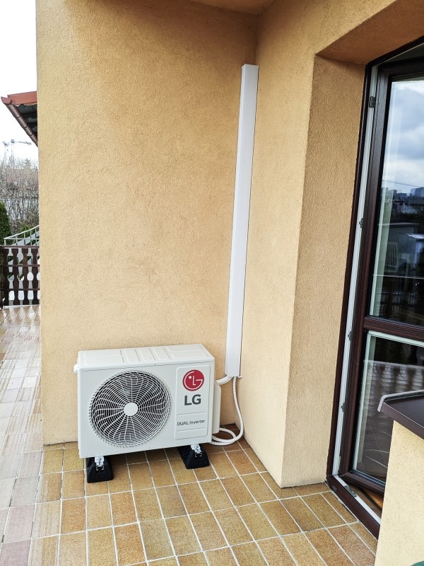 Zewnętrzna jednostka klimatyzacji LG Dual Inverter zamontowana na balkonie, z widocznymi wspornikami antywibracyjnymi i maskownicą przewodów.