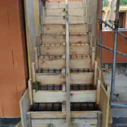 Szczegółowe ujęcie drewnianego szalunku schodów zbrojonych stalą, w trakcie budowy domu z cegły, z widocznymi elementami konstrukcyjnymi i rusztowaniem.