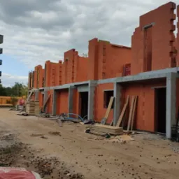 Budowa szeregowców z czerwonej cegły Porotherm. Widoczne pustaki, betonowe nadproża, drewniane deski i drabiny. Szary, pochmurny dzień.
