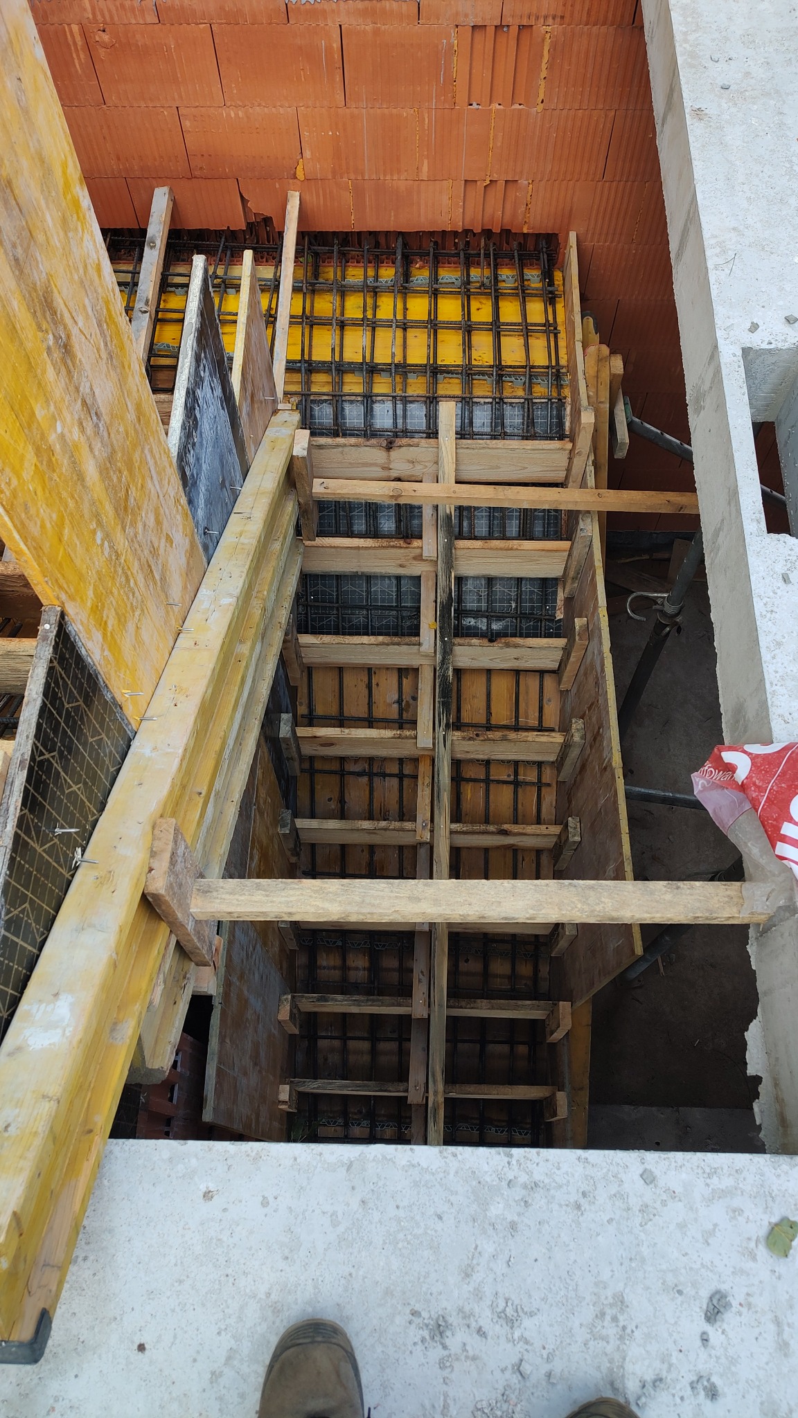 Szczegółowy widok z góry na drewniany szalunek zbrojony stalą, przygotowany pod wylewkę betonową; widoczne cegły stropowe.