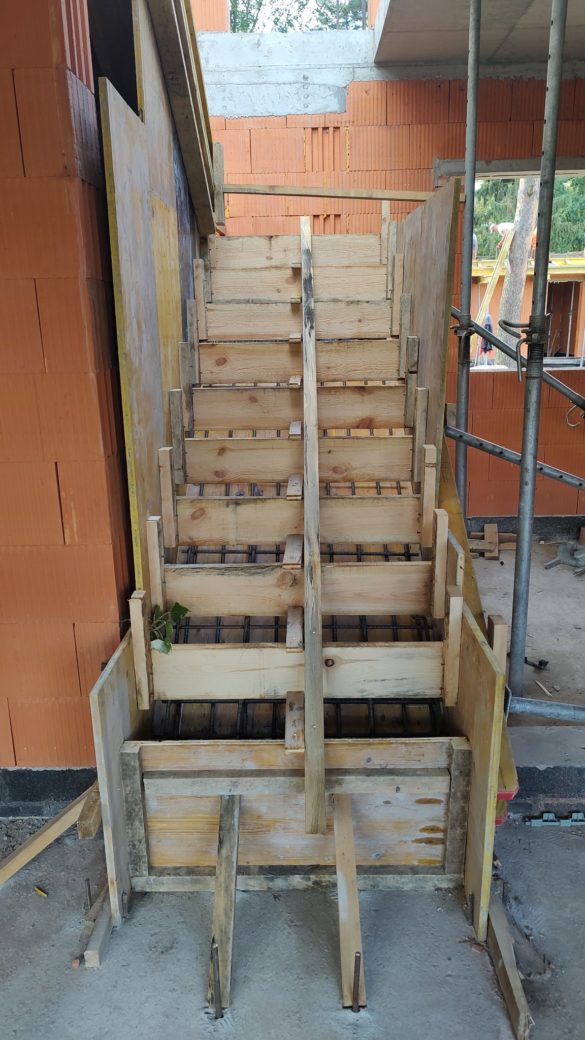 Szczegółowe ujęcie drewnianego szalunku schodów zbrojonych stalą, w trakcie budowy domu z cegły, z widocznymi elementami konstrukcyjnymi i rusztowaniem.