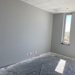 SV-BUD Serhii Vovk - Jasnoszary pokój po odświeżeniu, zabezpieczona folią podłoga, dwa okna z widokiem na zewnątrz i gniazdka elektryczne na ścianie. Minimalizm i świeżość.