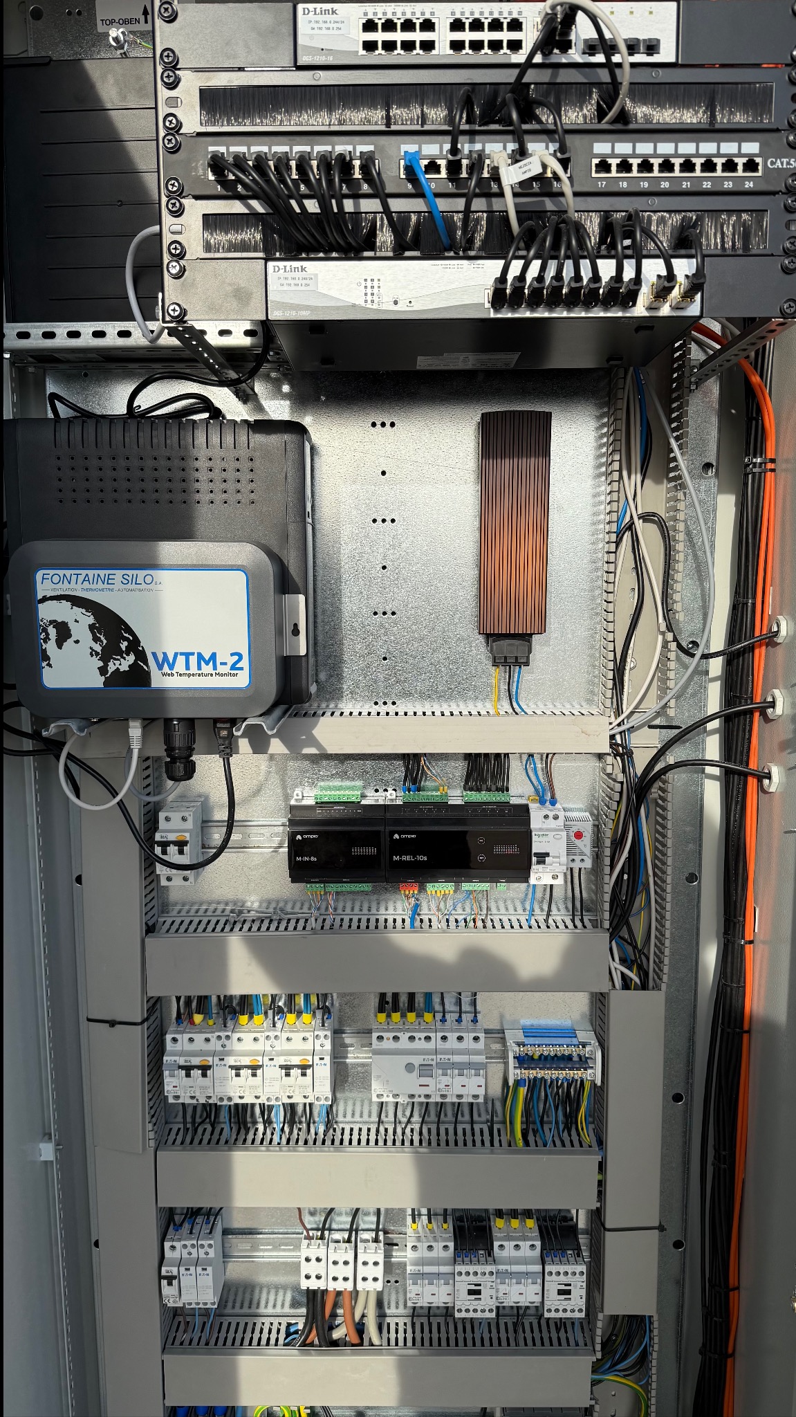 Rozdzielnica elektryczna z zamontowanymi urządzeniami sterującymi, przełącznikami sieciowymi D-Link, modułem monitoringu temperatury Fontaine Silo WTM-2, zabezpieczeniami i okablowaniem.