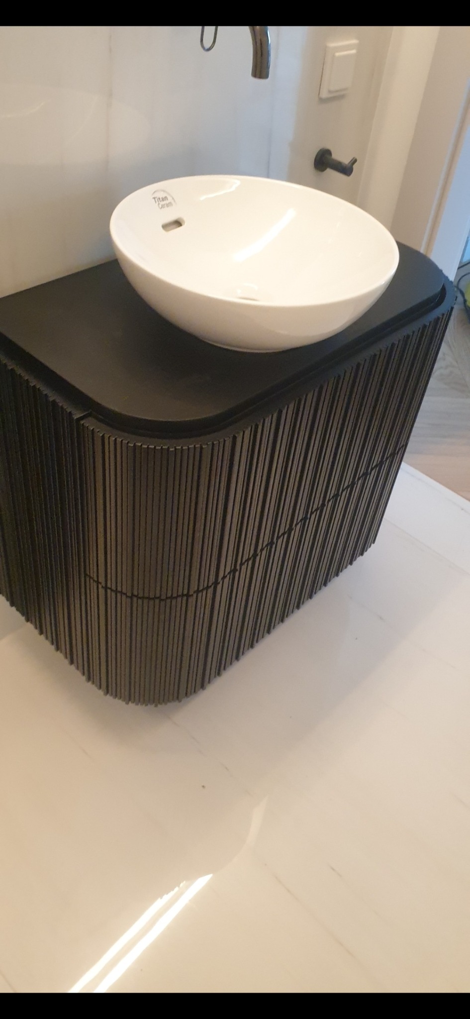 Nowoczesna szafka łazienkowa z umywalką nablatową. Szafka w kolorze ciemnego drewna z unikalnym, żłobionym frontem. Minimalistyczny design, jasne tło.