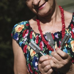 Gabinet Naturoterapii - Kobieta z uśmiechem trzymająca w dłoniach trzy kamertony, narzędzia używane w terapii dźwiękiem. Widoczny kwiecisty strój i czerwone korale.
