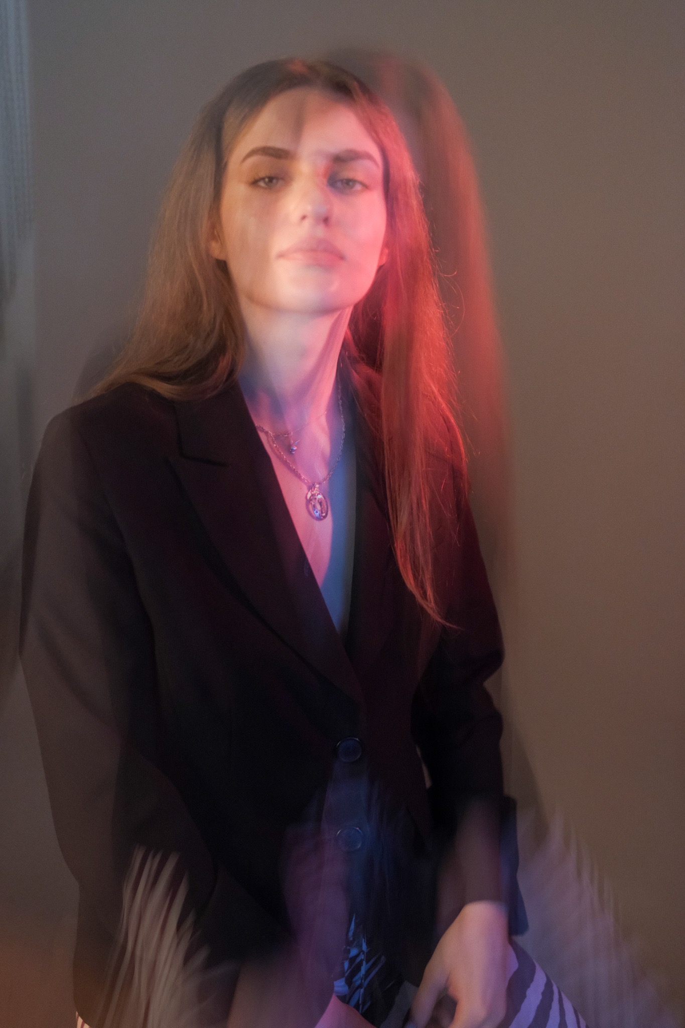 Portret kobiety w czarnej marynarce z naszyjnikiem, oświetlonej kolorowymi światłami, wykonany w Popielowskiej Kolonii. Nietypowe oświetlenie i artystyczne rozmycie.