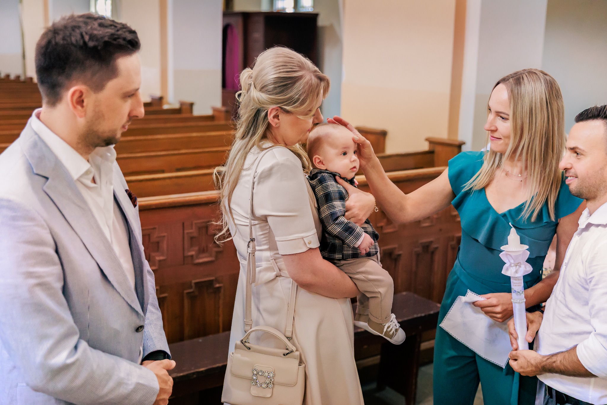 Uroczystość chrztu w kościele: matka trzyma dziecko, a goście gratulują. W tle drewniane ławki i dekoracje. Ciepłe, naturalne światło podkreśla intymny charakter wydarzenia.