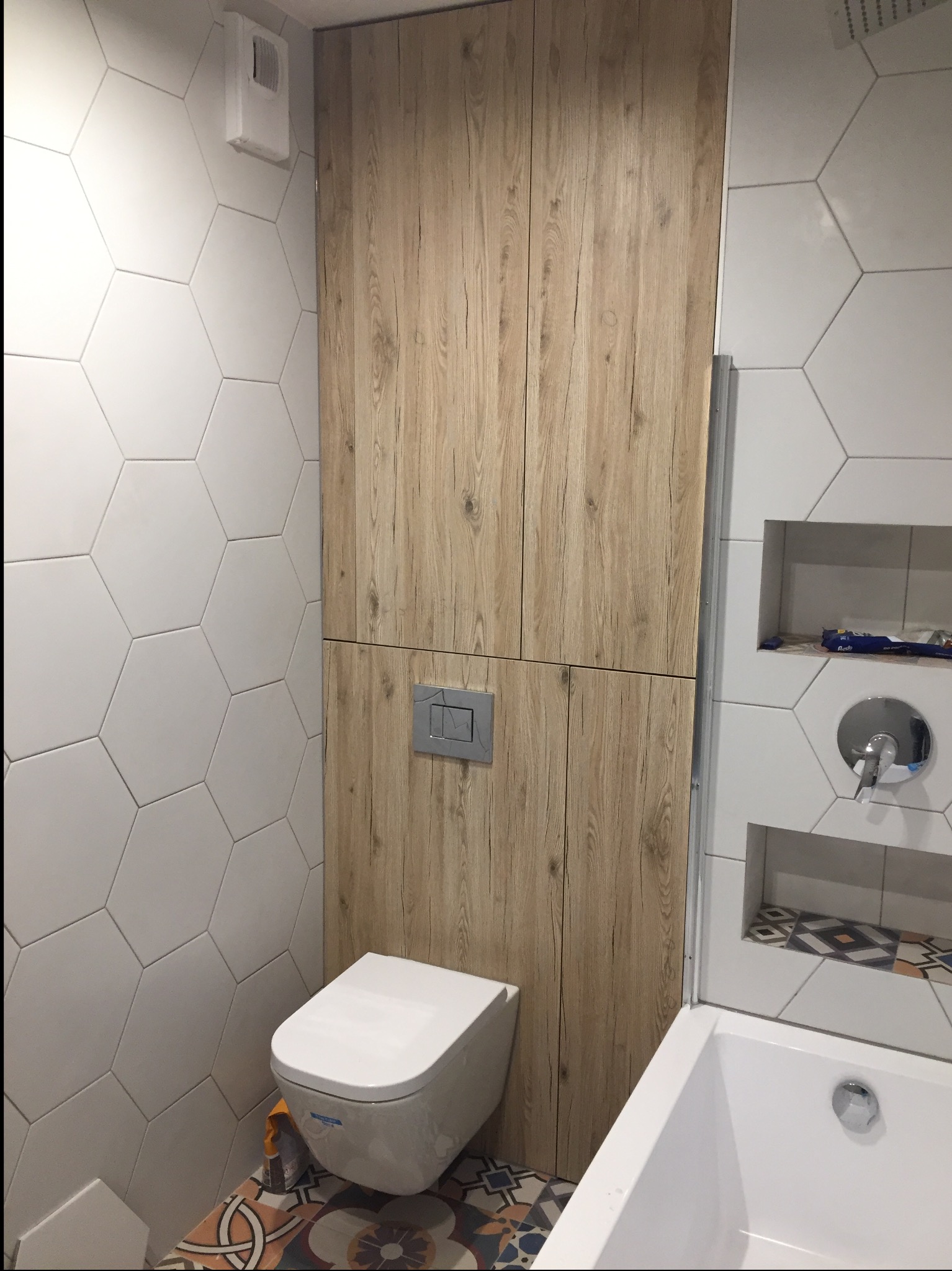 Nowoczesna łazienka z wiszącą toaletą, zabudową z drewnopodobnych paneli i heksagonalnymi płytkami na ścianach.