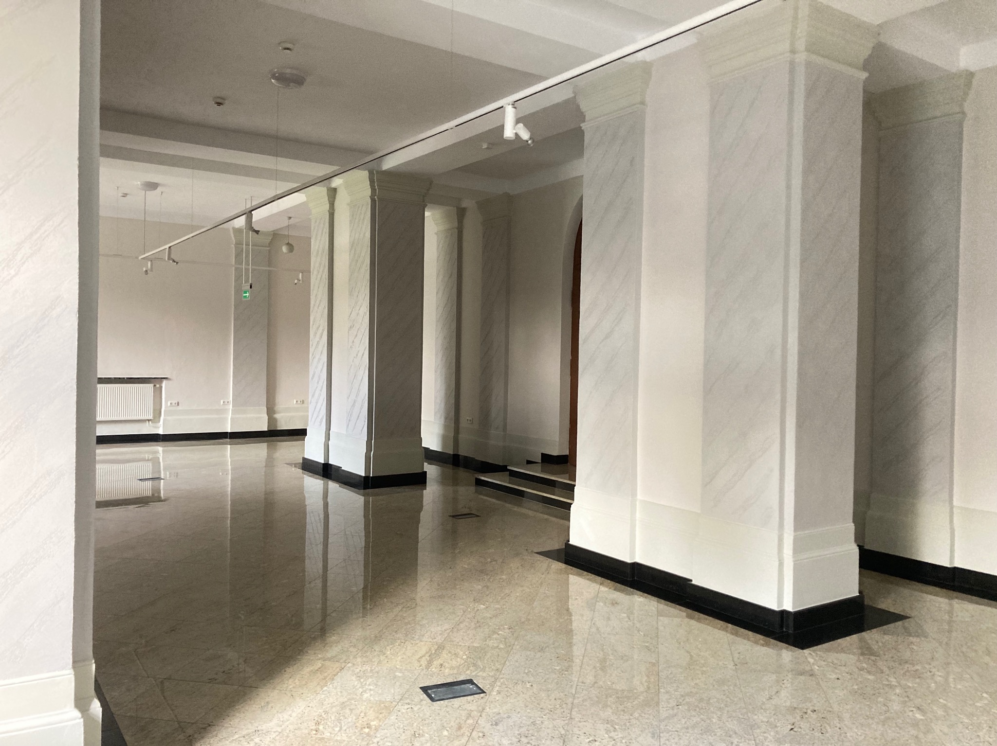 Wnętrze przestronnego holu z marmurowymi kolumnami, polerowaną podłogą i nowoczesnym oświetleniem szynowym.
